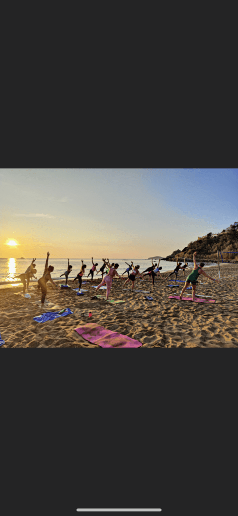 Group of people doing yoga on a beach at sunrise